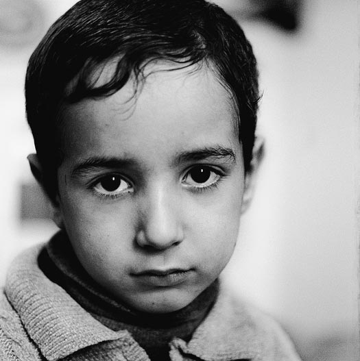 A young boy, his head tilted downward, looks up at the camera.