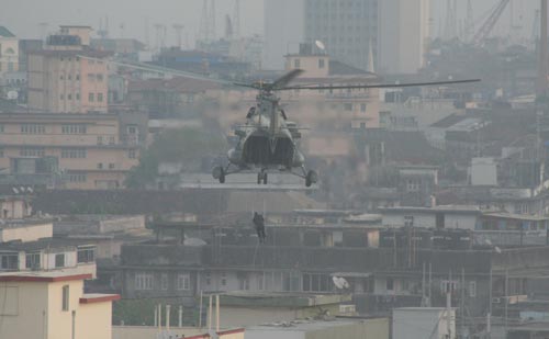 A man slides down a rope from a large helicopter onto the roof of a building.