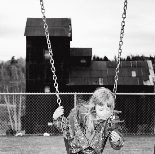 Lola Angus on a swing in the grade school playground adjacent to the Right of Way Mine property, Cobalt, Ontario.