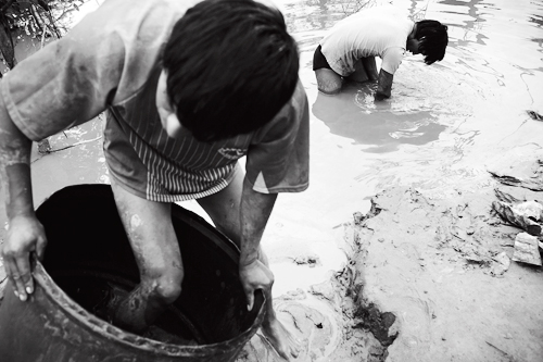 A mineworker climbs barefoot into a barrel filled with sediment and mercury.