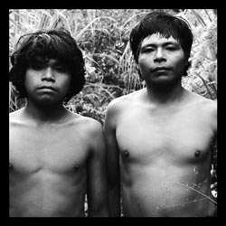 Two bare-chested men stand side by side. One is an adolescent—still a boy, really—with a mop of black hair while the other could be anywhere from twenty to forty years in age. Both gaze into the camera.