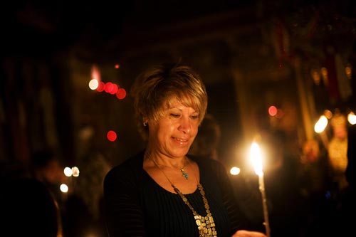 A smiling, middle-aged woman looks down at the lit taper in her hand.
