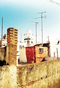 An eight-sided tower can be seen amidst the clutter of rooftop antennae, chimneys, and walls.