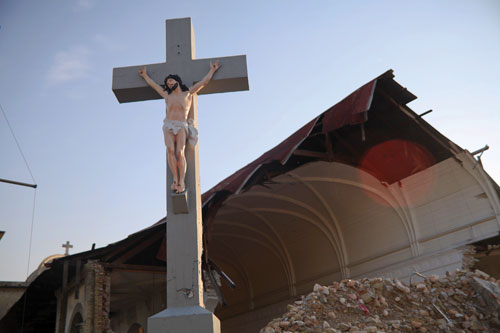A crucifix stands in front of a pile of rubble from a demolished building.