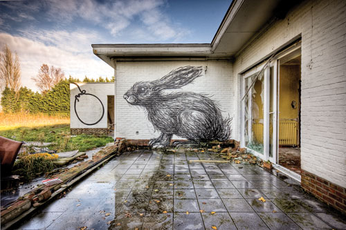 An abandoned house with broken sliging glass doors with a giant rabbit graffittied onto the wall.