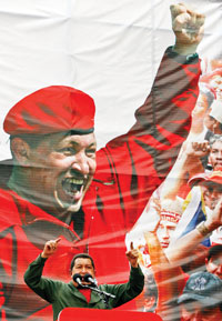Hugo Chavez speaking in front of a large banner with an image of himself in red.