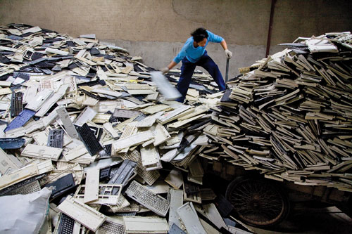 A woman unloads a cart stacked high with empty computer keyboard casings.