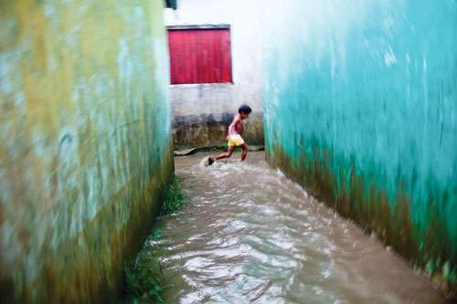 A child runs through a rush of water flowing between buildings after a downpour.
