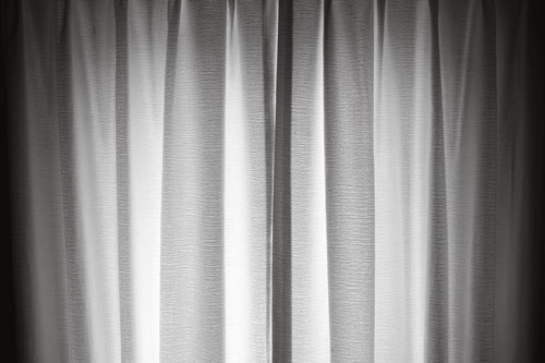 A black and white image of a window with light illuminating the curtains from outside.