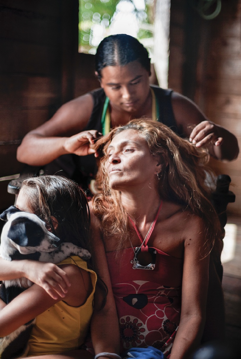 Jamaica picks lice from Nazaré’s hair as Nazaré’s daughter (L) plays with their new dog. Nazaré sold goods on the cargo ships for some years until her husband Lucevaldo stopped her. Now the family survives on his earnings trading oil. 