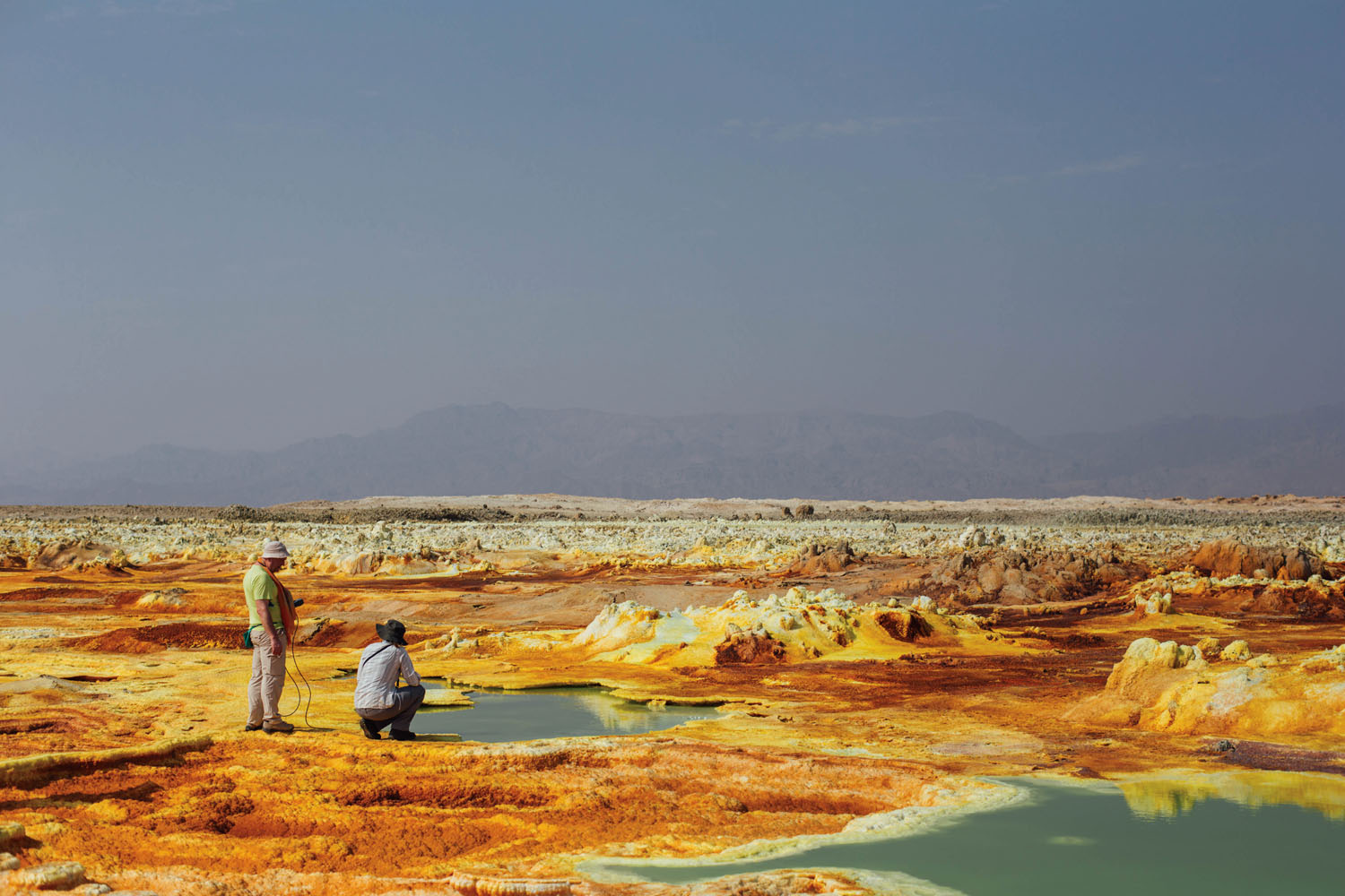 Dutch researchers kneel next to a sulfur pool at Dallol, Ethiopia. The extreme heat, acidity, and sulfur content at Dallol make it an excellent research site for scientists studying the limits of life, both here on Earth and elsewhere in the solar system. Photograph by Alex Pritz.