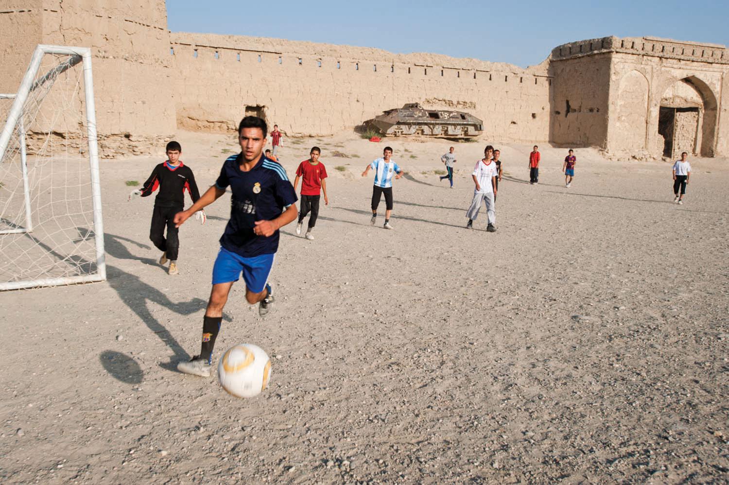 Young men play football before school on a hill overlooking Kabul, beside an ancient mudbrick fortress and the rusting hulk of a Soviet armored personnel carrier.