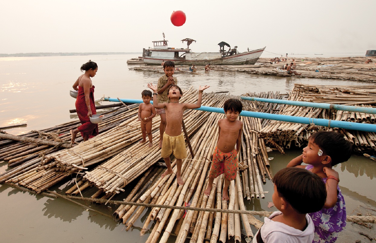 Children play ball on a bamboo raft along the Mandalay quai. Lashed together upriver, the makeshift rafts are floated down to the boomtown and used as construction scaffolding. Photo by Jason Motlagh.