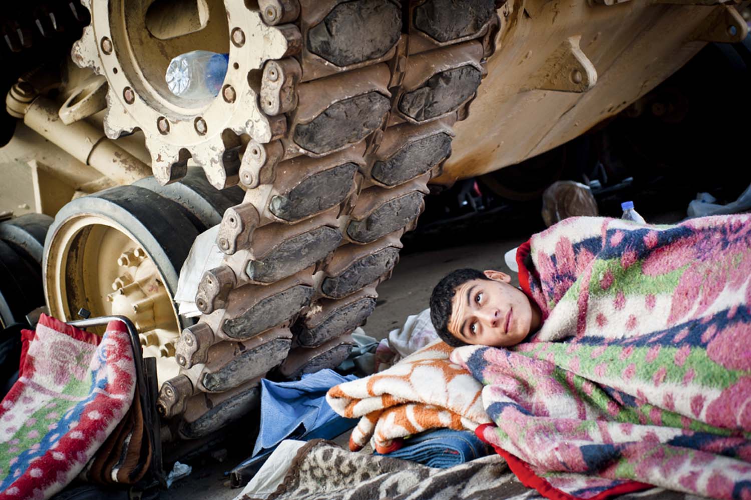 A boy rests under the treads of an Egyptian army tank in Tahrir Square, in downtown Cairo. Protesters gathered there beginning on January 25, 2011, calling for the ouster of President Hosni Mubarak, who had ruled the country unopposed since 1981