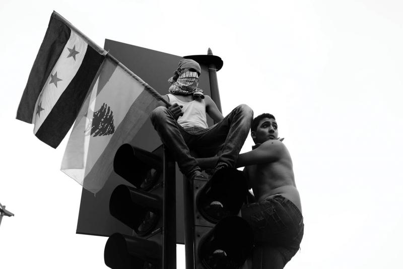 Men perched on a traffic light during the protest, raising both the Syrian and Lebanese flags. From Alex Potter's "After the Funeral."