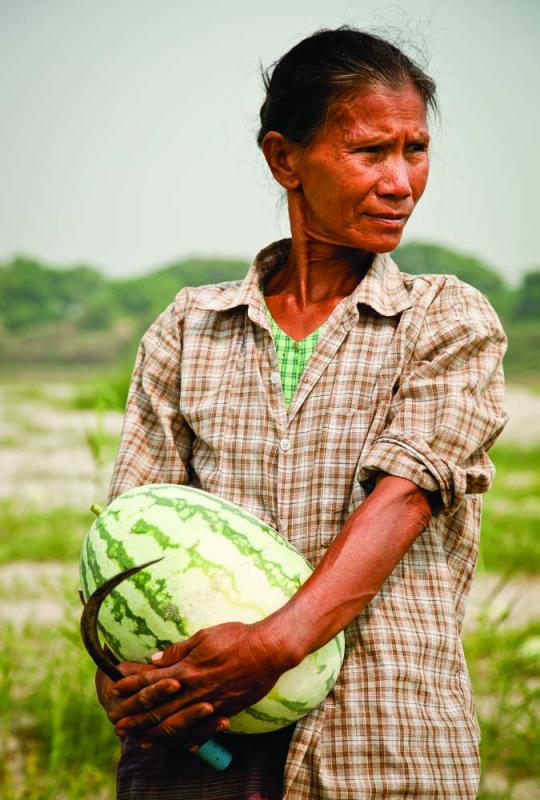 Daw Paw, 52, farmer and grandmother, clutches a water­melon pulled from a seasonal plot her family rents from the government. A small tax is paid on their harvest. Photo by Jason Motlagh.