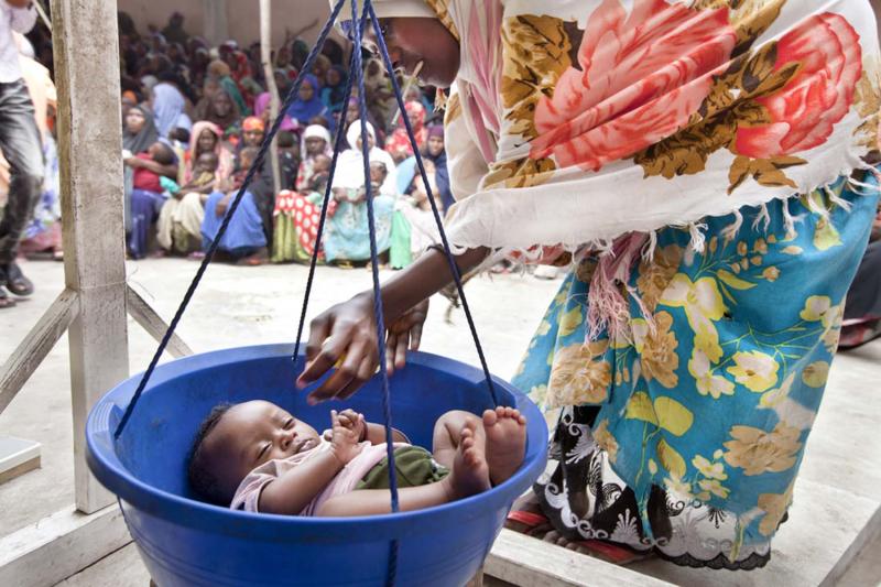 A mother places her infant into a plastic tub, suspended from a hanging scale, at a Saacid healthcare center in Mogadishu.
